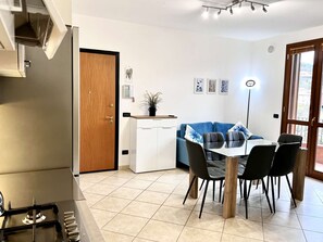Une cuisine moderne équipée d’une cuisinière à gaz, un coin repas avec une table et des chaises, une porte en bois et une vue par la fenêtre.