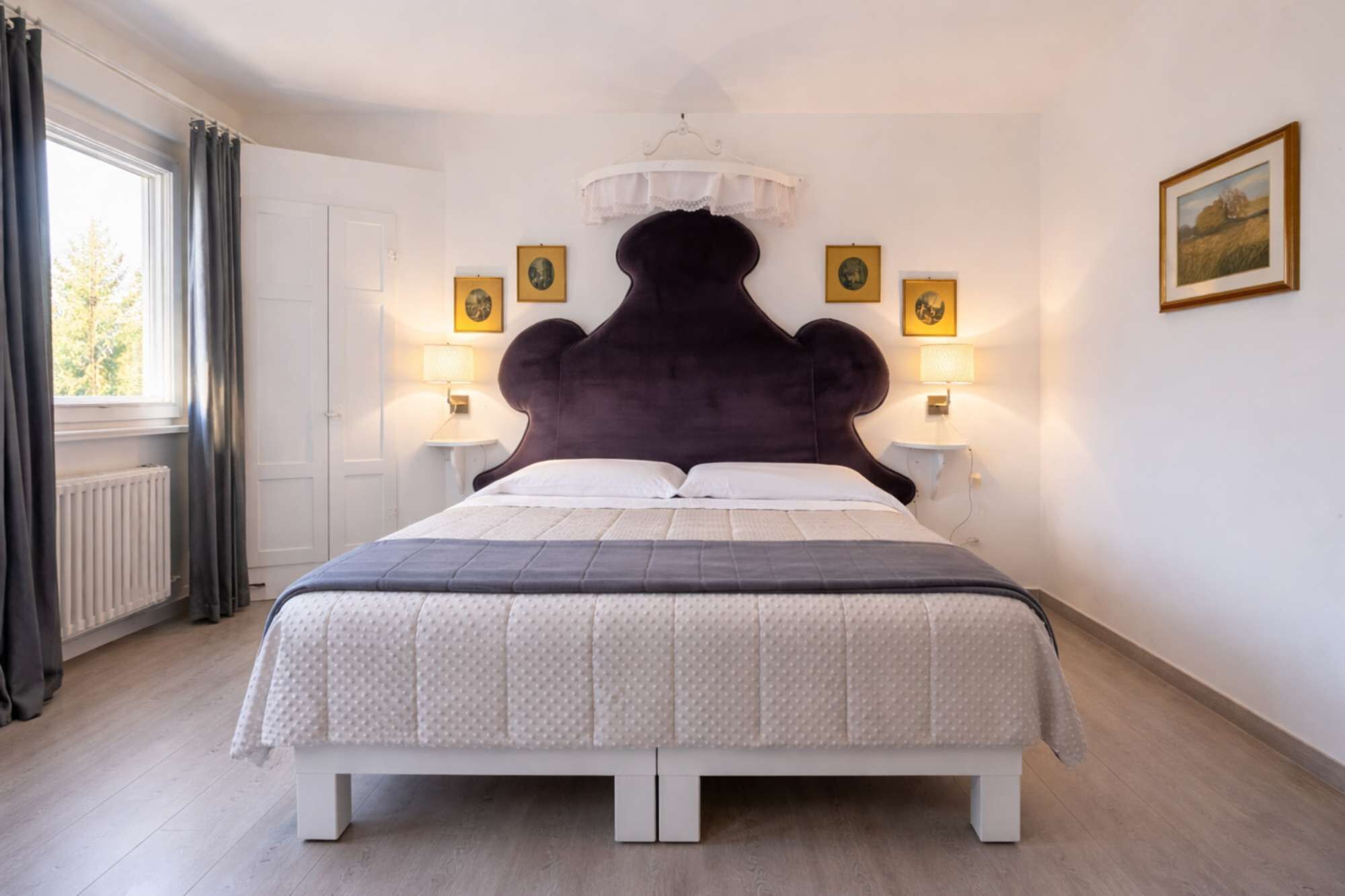 Un dormitorio con una cama grande, dos lámparas de noche, una ventana con cortinas y un cuadro en la pared.