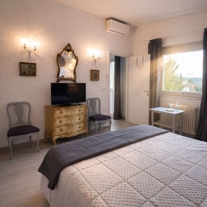 Ein Hotelzimmer mit Bett, Fernseher, Kommode, Sessel und Schreibtisch mit Fenster.