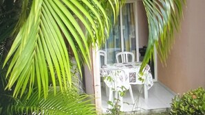 A covered outdoor seating area with a table and chairs, surrounded by lush green foliage. - Ti Case Sainte Anne, Martinique (Sainte-Anne)