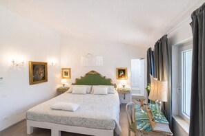 Ein Hotelzimmer mit einem großen Bett, zwei Nachttischen, einem Sessel, einem Fenster mit Vorhängen und Wandlampen.