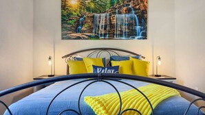 A bedroom with a bed, a headboard, a painting of a waterfall, and two bedside lamps. - No stairs, clean peaceful secluded, close to strip (Branson)