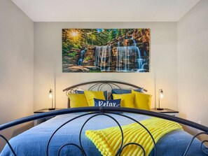 A bedroom with a bed, a headboard, a painting of a waterfall, and two bedside lamps. - No stairs, clean peaceful secluded, close to strip (Branson)