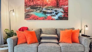 A living room with a grey sofa, orange cushions, a wooden coffee table, and a painting of a waterfall. - No stairs, clean peaceful secluded, close to strip (Branson)