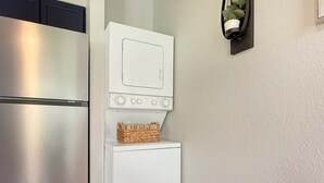 A compact kitchen with a stainless steel refrigerator, a white washing machine, and a small basket on top. - No stairs, clean peaceful secluded, close to strip (Branson)