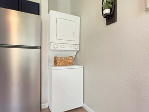 A compact kitchen with a stainless steel refrigerator, a white washing machine, and a small basket on top. - No stairs, clean peaceful secluded, close to strip (Branson)