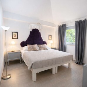 Ein Schlafzimmer mit einem großen Bett, zwei Nachttischen, einer Stehlampe und einem Fenster mit Vorhängen.