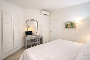 Ein Schlafzimmer mit Bett, Schreibtisch mit Computer, Stuhl, Spiegel und einem Bild an der Wand.