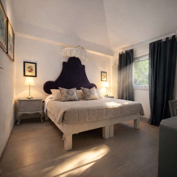 Ein Schlafzimmer mit einem großen Bett, zwei Nachttischen mit Lampen, einem Fenster mit Vorhängen und gerahmten Bildern an der Wand.