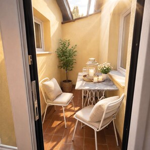 Eine kleine Terrasse mit zwei weißen Stühlen, einem Tisch mit Kerzen, einem Laternen und einem Blumentopf.