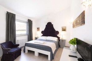 Ein Schlafzimmer mit Bett, Nachttischen, einem Sessel, einem Fernseher und einem Fenster mit Vorhängen.