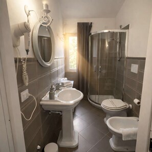 Ein Badezimmer mit einem Standwaschbecken, einer Toilette, einer Duschkabine und einem Spiegel.