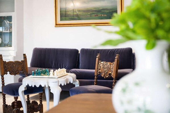 Ein Wohnzimmer mit einem dunkelgrauen Sofa, einem weißen Couchtisch mit Schachfiguren und einem dekorativen Sessel.