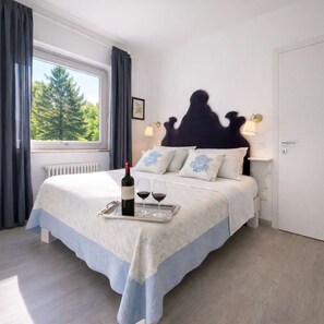 Ein Schlafzimmer mit Bett, Fenster, Heizkörper und einer Weinflasche auf einem Tablett.