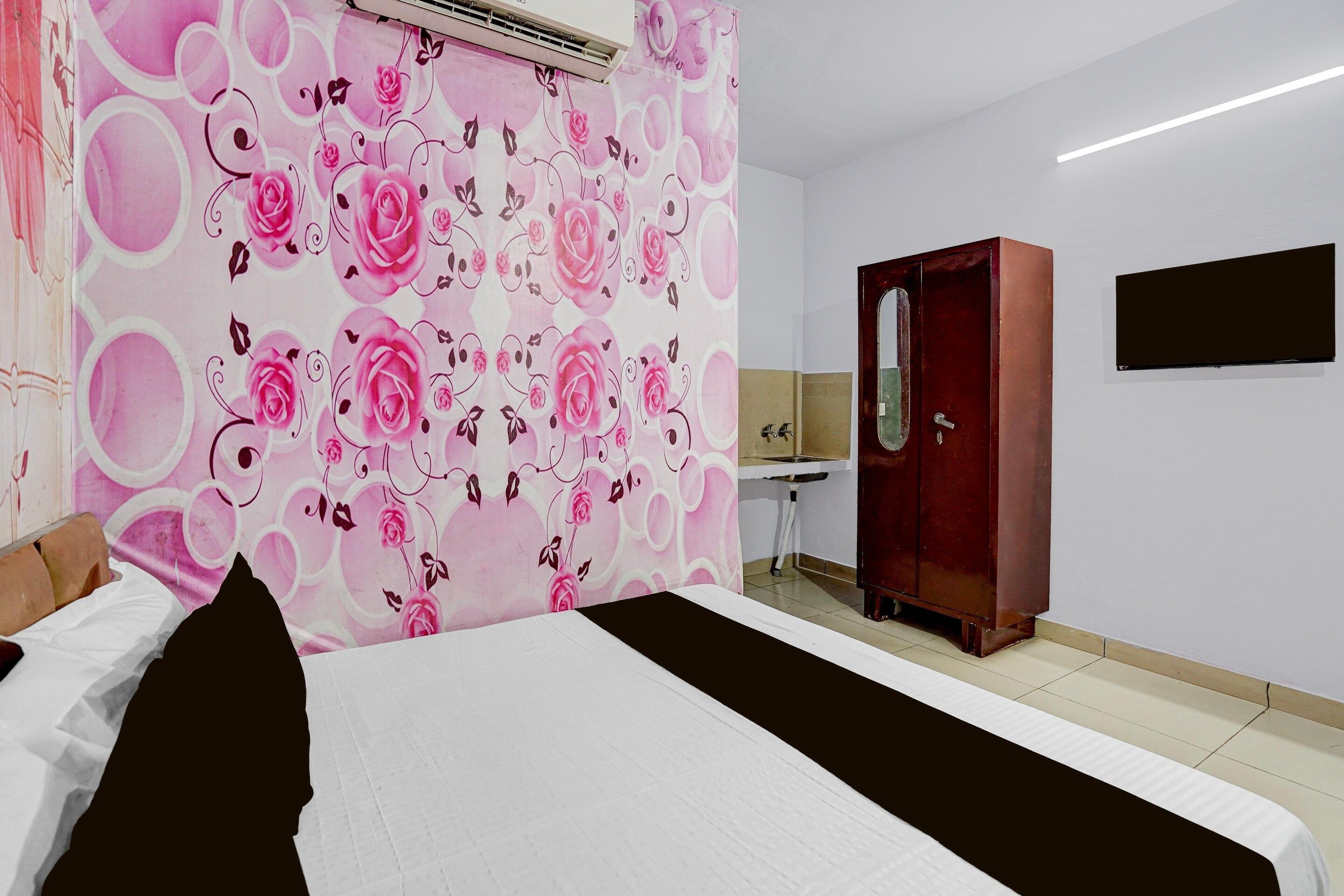 A hotel room with a bed, a desk, a wardrobe, and a wall with a floral pattern.