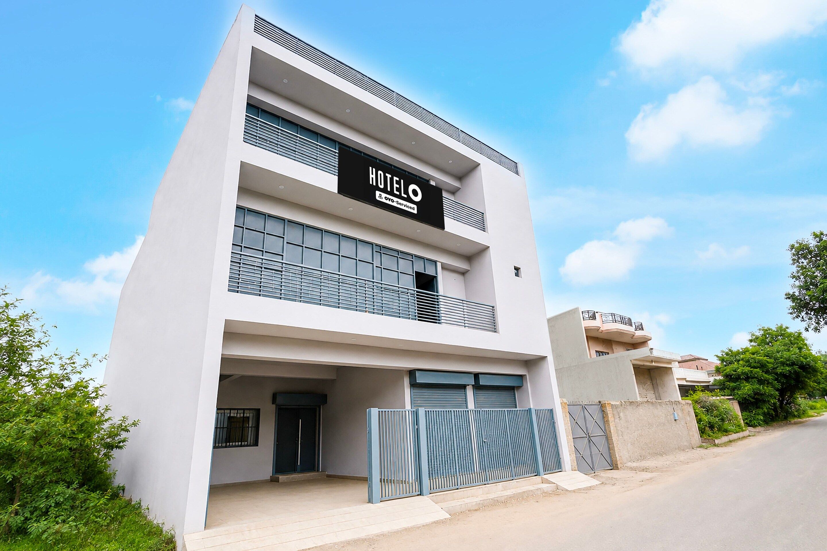 A modern hotel building with a prominent sign, a gated entrance, and a clear sky.