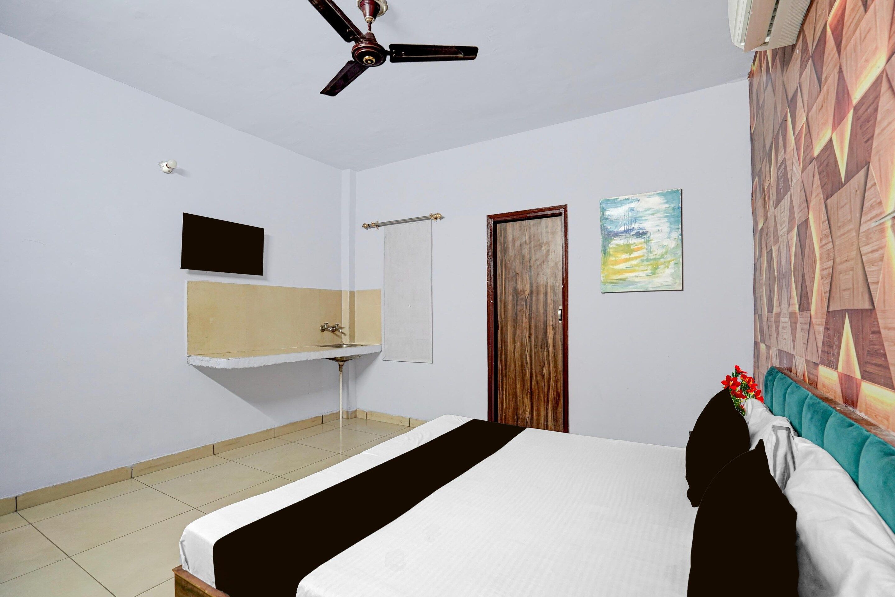 Un dormitorio con cama, ventilador de techo, lavamanos, espejo y una puerta.
