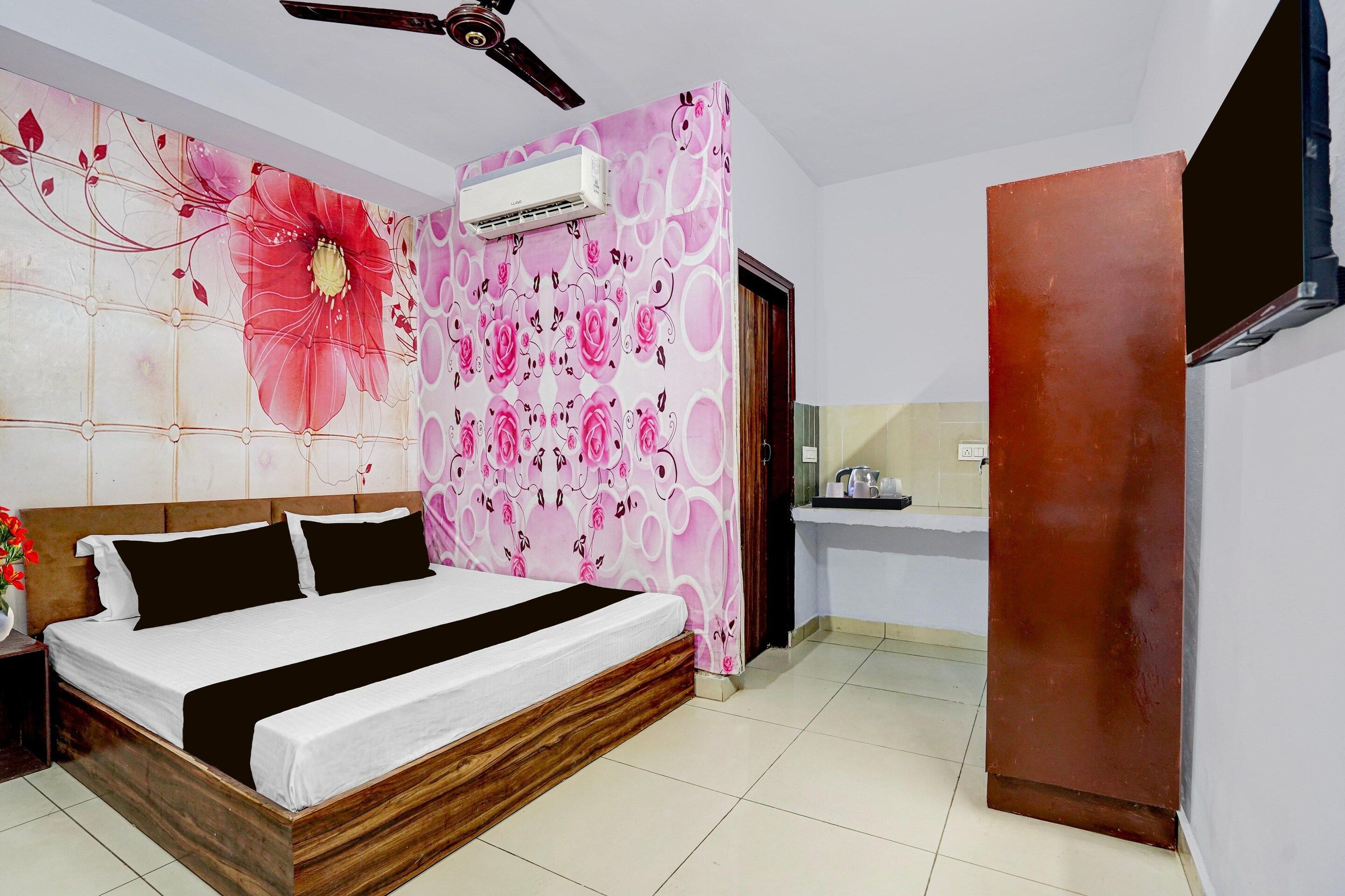 A bedroom with a bed, a ceiling fan, an air conditioning unit, and a bathroom with a sink and mirror.