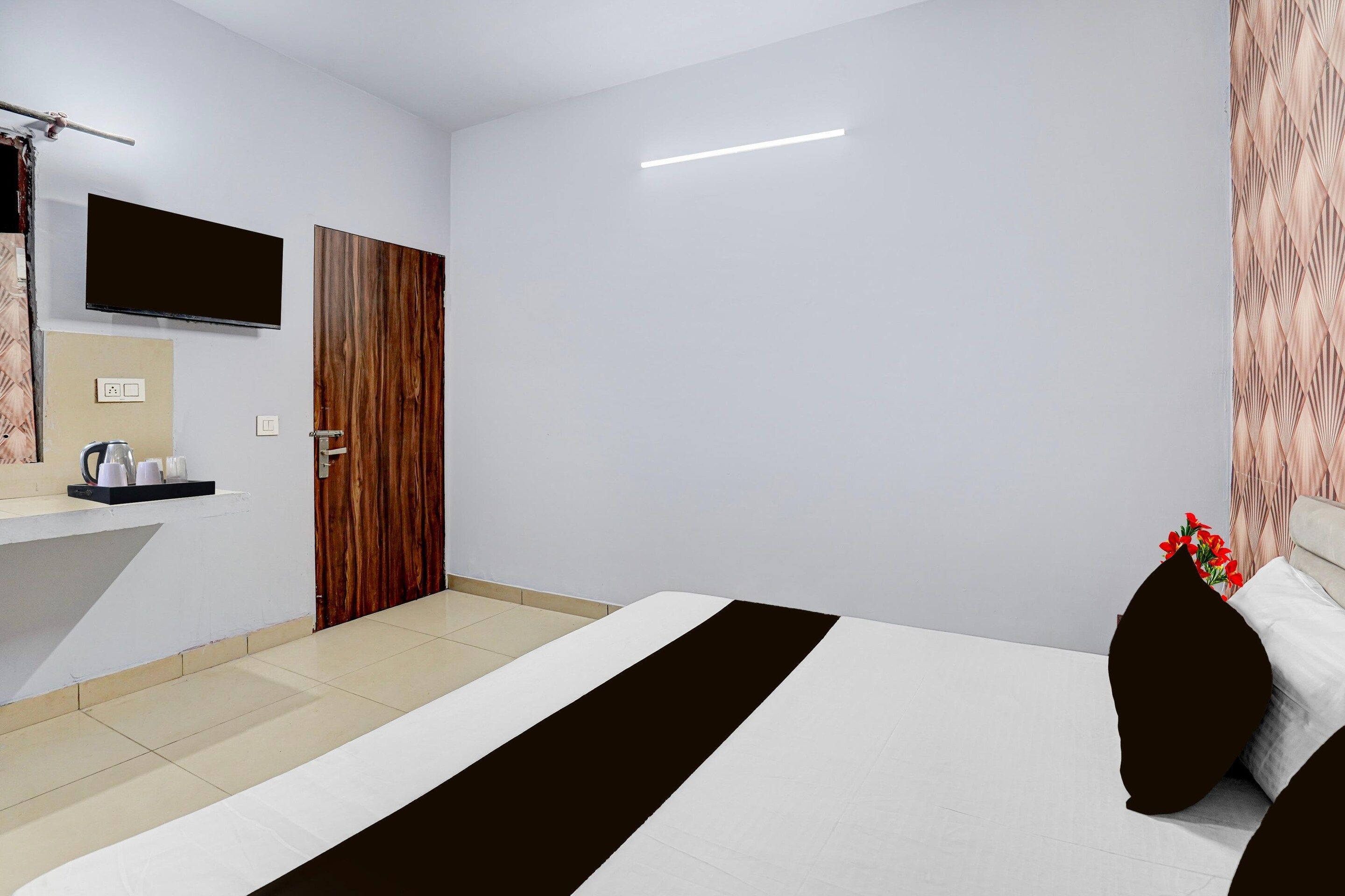 A hotel room with a bed, a flat-screen TV, a wooden door, and a bathroom area with a sink and mirror.