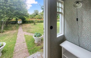 A view of a garden with a stone pathway leading to a door, and a white interior with floral wallpaper and a ceiling light fixture. - 2 bedroom lovely home in Ljungbyholm (Ljungbyholm)