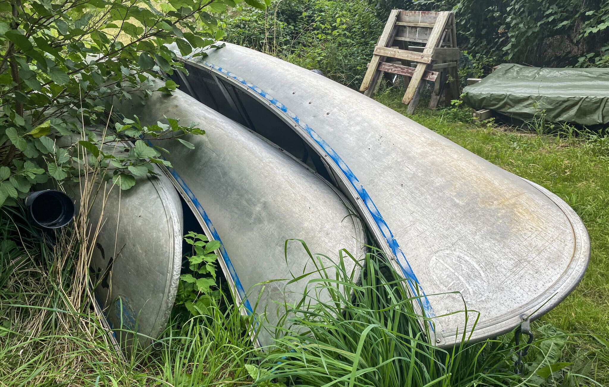 A large metal structure, possibly a slide, in a grassy area with a wooden ladder and a tarp nearby.