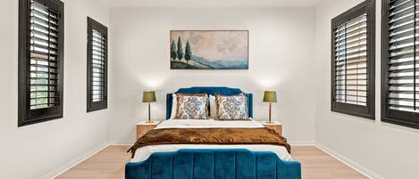 A bedroom with a large bed, two bedside tables, a painting on the wall, and a window with blinds.