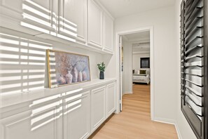 A hallway with white paneling, a painting of vases, and a potted plant. - Luxury 7BR Getaway/10 Beds/Near Victoria Gardens (Rancho Cucamonga)