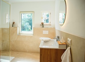 A modern bathroom with a glass shower enclosure, a large sink, and a window providing natural light. - Villa Ardoise (Brodenbach)