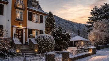 Una casa de dos pisos con una escalera de piedra que conduce a la entrada, rodeada de árboles cubiertos de nieve y una montaña al fondo.