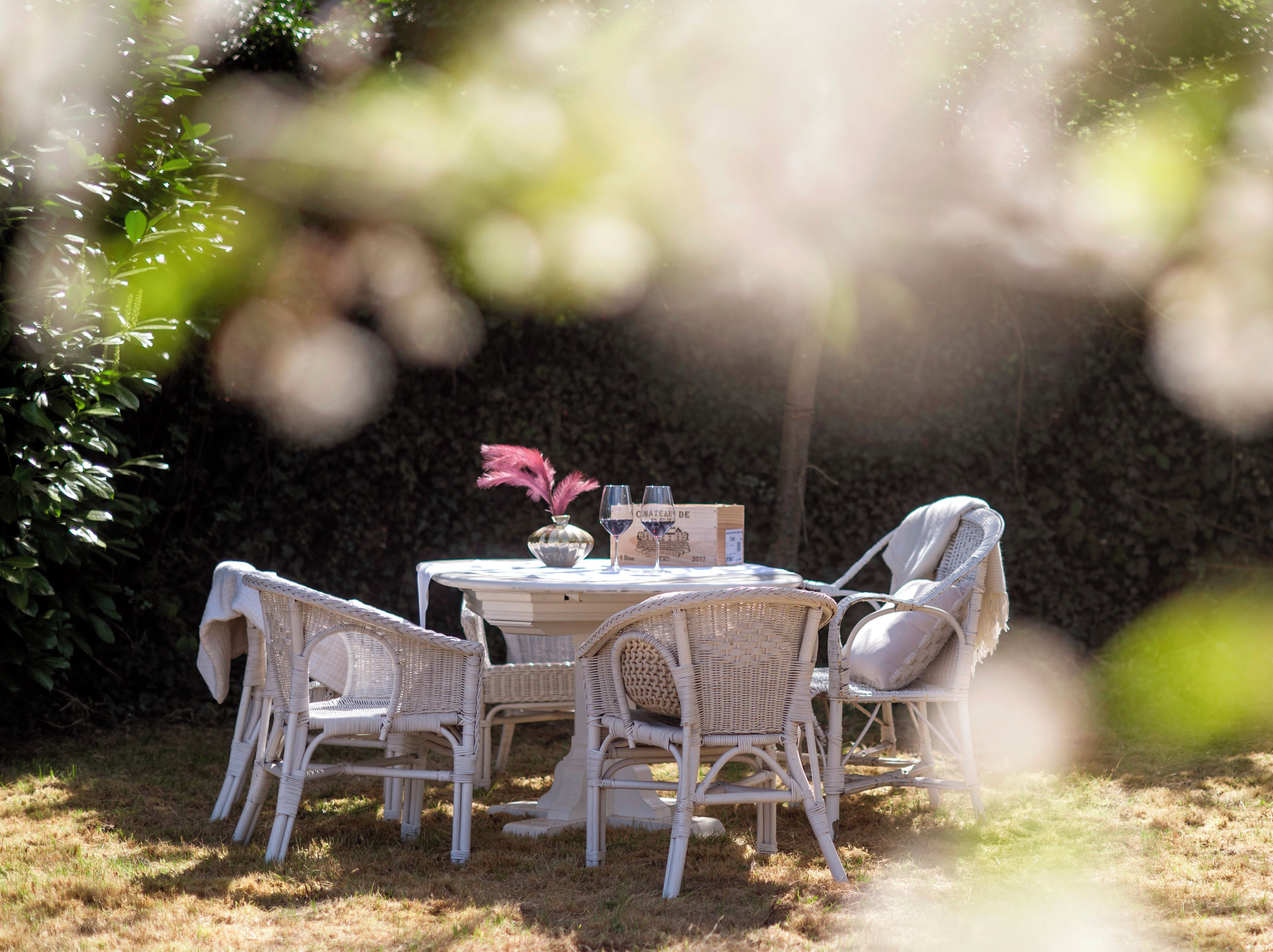 Un área de estar al aire libre con sillas de mimbre y una mesa, rodeada de follaje.