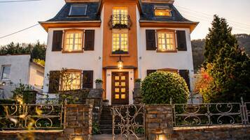 A two-story house with a central entrance, a balcony, and a stone wall with a gate.