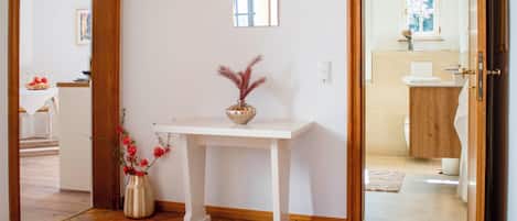 A hallway with a white console table, a mirror, and a vase with red flowers.