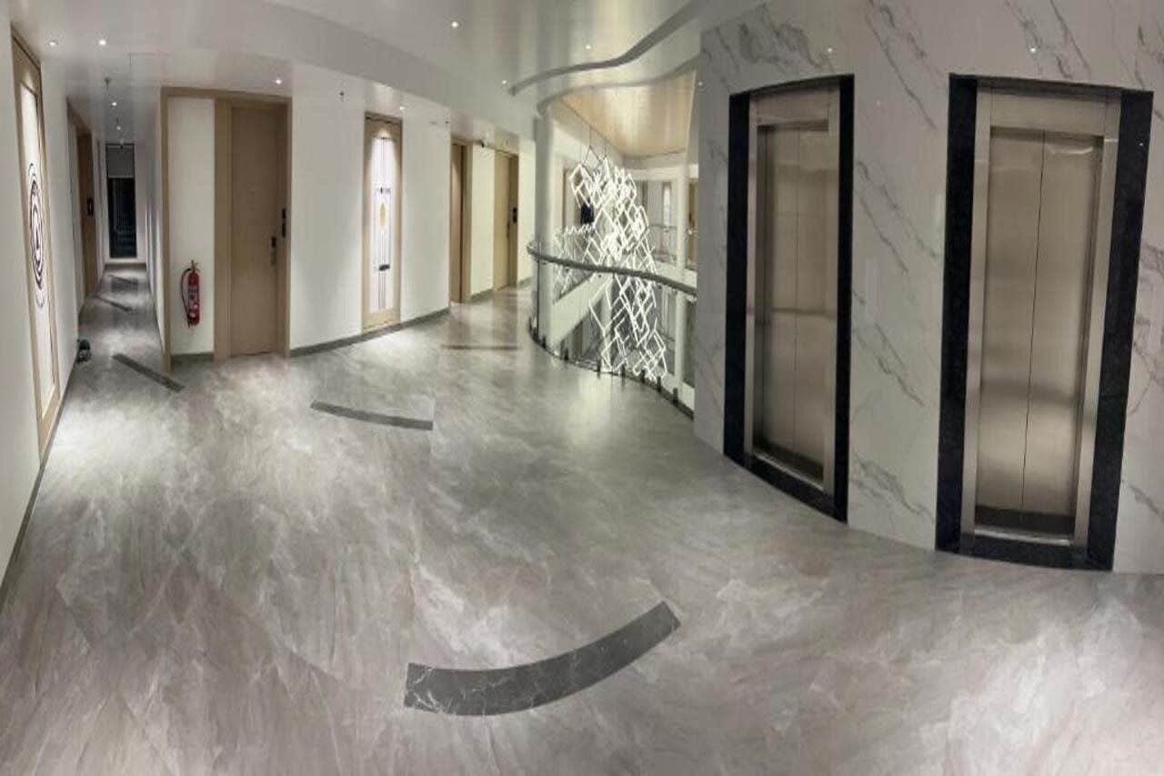 A modern hotel corridor with marble flooring, glass railings, and elevators.