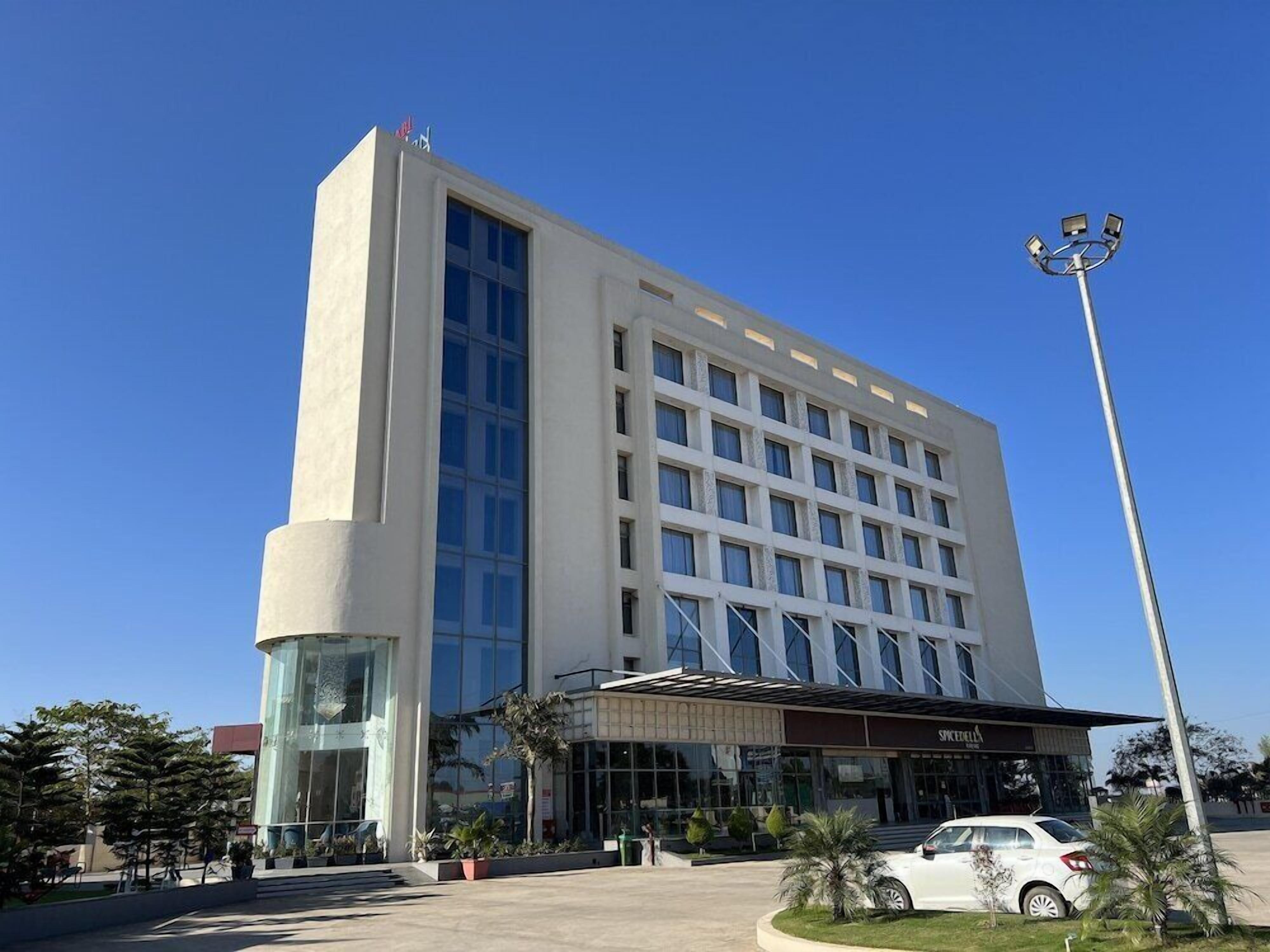 A modern hotel with a prominent glass facade, a covered entrance, and a parking area.