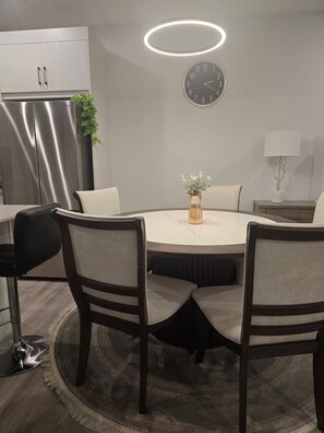 A modern dining area with a round table, four chairs, a clock, a refrigerator, and a plant. - Modern Spacious Home - Near Airport (Northeast)