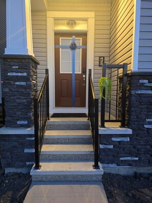 A front entrance with a brown door, stone steps, and a black railing. - Modern Spacious Home - Near Airport (Northeast)