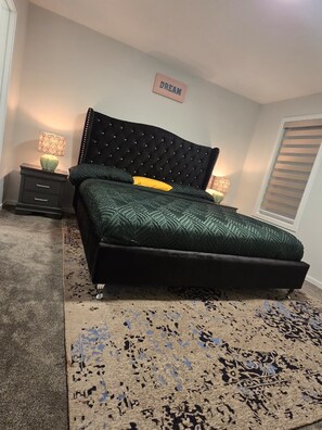 A bedroom with a tufted headboard, a patterned bedspread, two bedside lamps, a rug, and a wall sign that reads 'DREAM'. - Modern Spacious Home - Near Airport (Northeast)