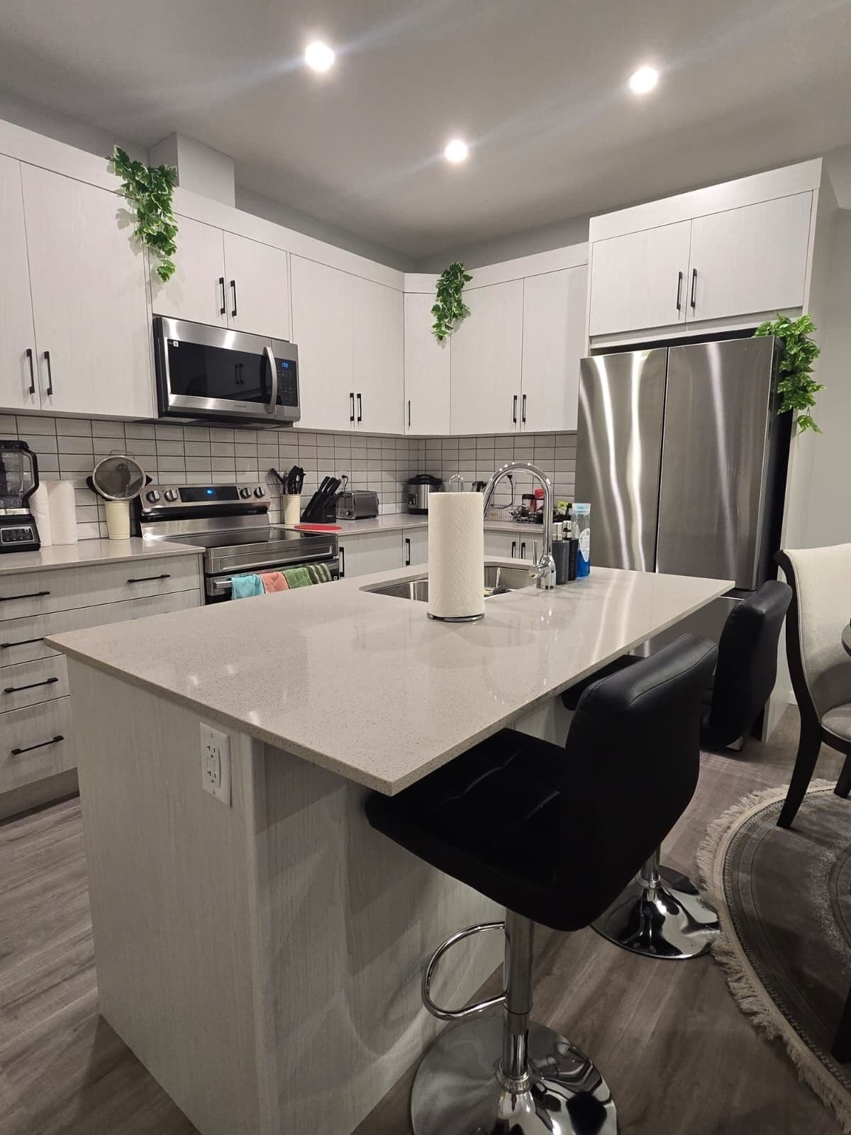 A modern kitchen with white cabinets, stainless steel appliances, a central island with bar stools, and a built-in microwave.