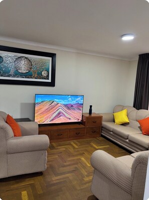 Ein Wohnzimmer mit zwei gemusterten Sofas, einem Flachbildfernseher, einem Holzschrank und einem gerahmten Kunstwerk an der Wand.