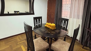 A dining area with a round glass table, four chairs, a mirror, and a window with curtains. - Apartment in the Amauta 121 Housing Complex (Cusco)