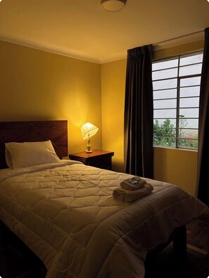 Ein Hotelzimmer mit Bett, Nachttisch, Lampe und einem Fenster mit Vorhängen.