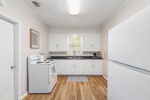 Cocina compacta con gabinetes blancos, estufa y ventana con persianas.