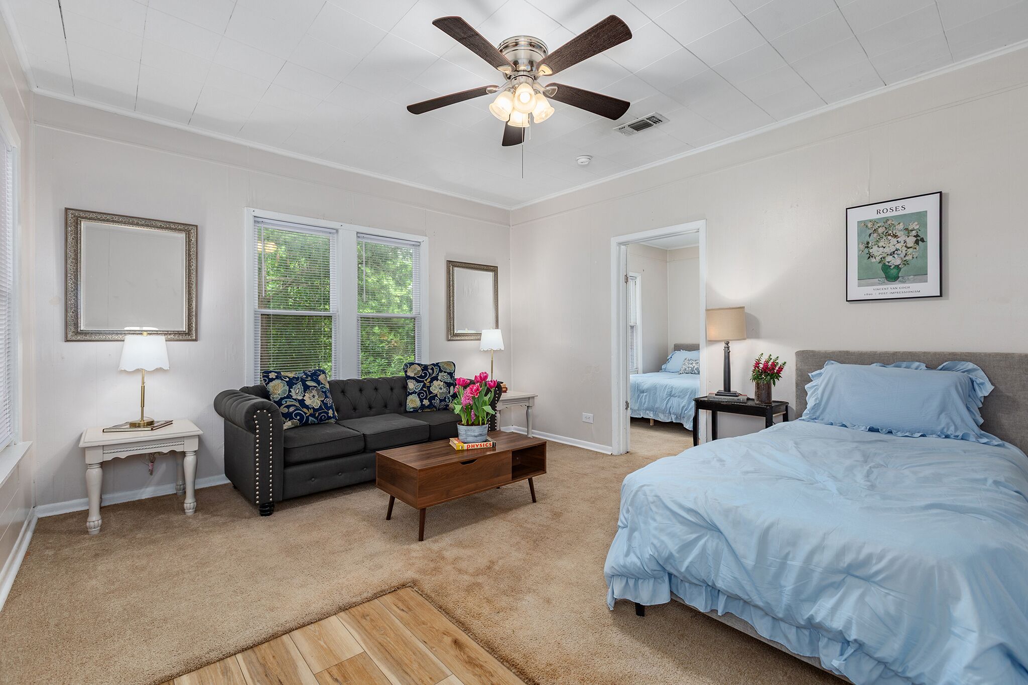 A bedroom with a bed, a sofa, a coffee table, and a ceiling fan.