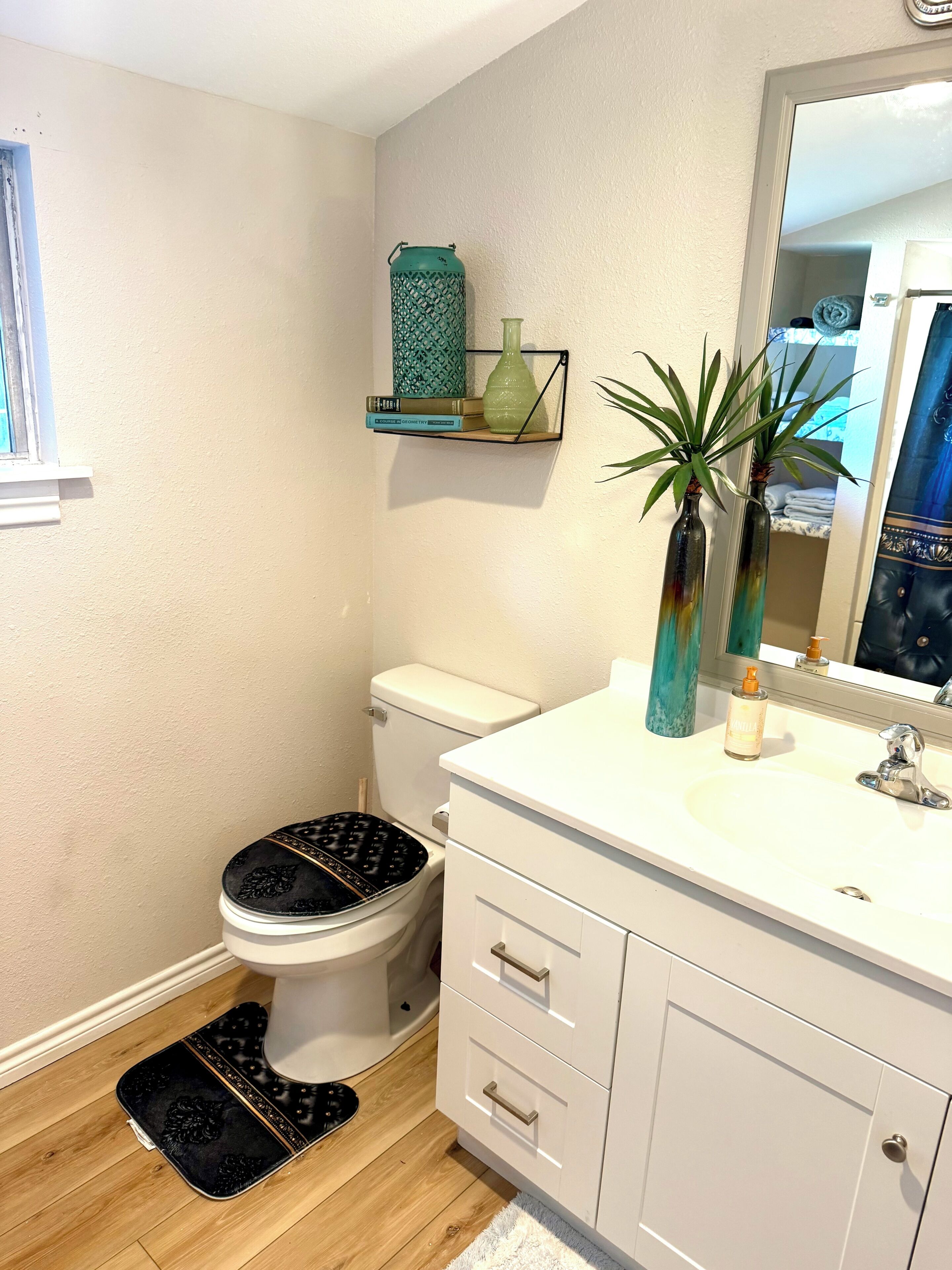 A bathroom with a toilet, a sink, a mirror, and a shelf with decorative items.