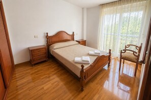 A neatly made bed with a wooden headboard, a wooden nightstand, a chair, and a window with curtains.