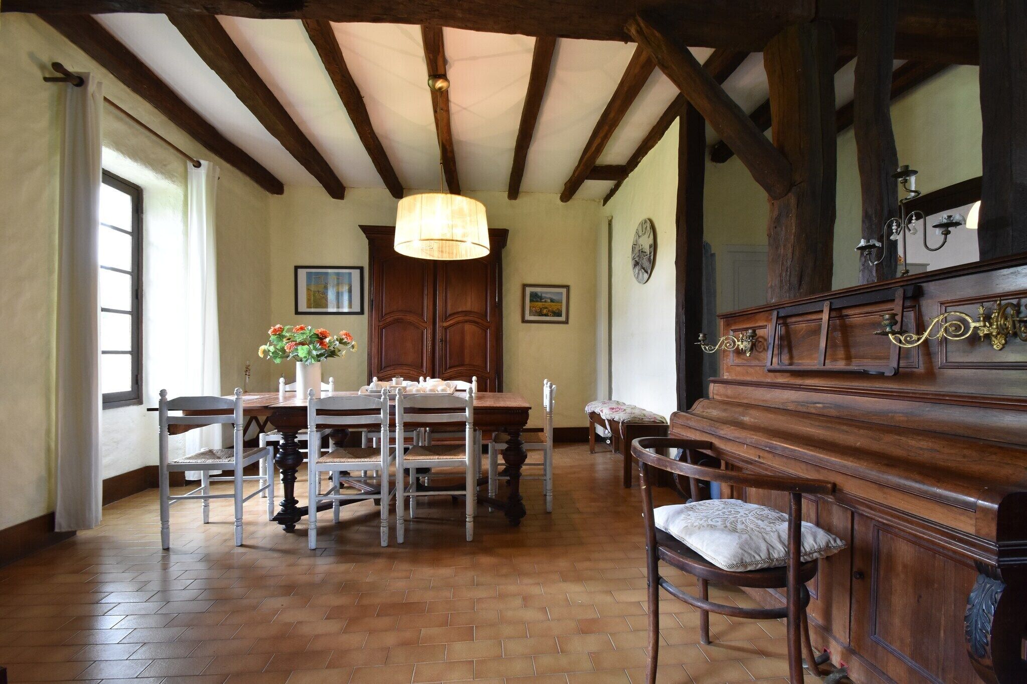 A dining room with a wooden table and chairs, a chandelier, and a piano.