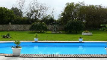 Une piscine dotée d’une terrasse en bois, entourée d’un mur de pierre et de verdure.