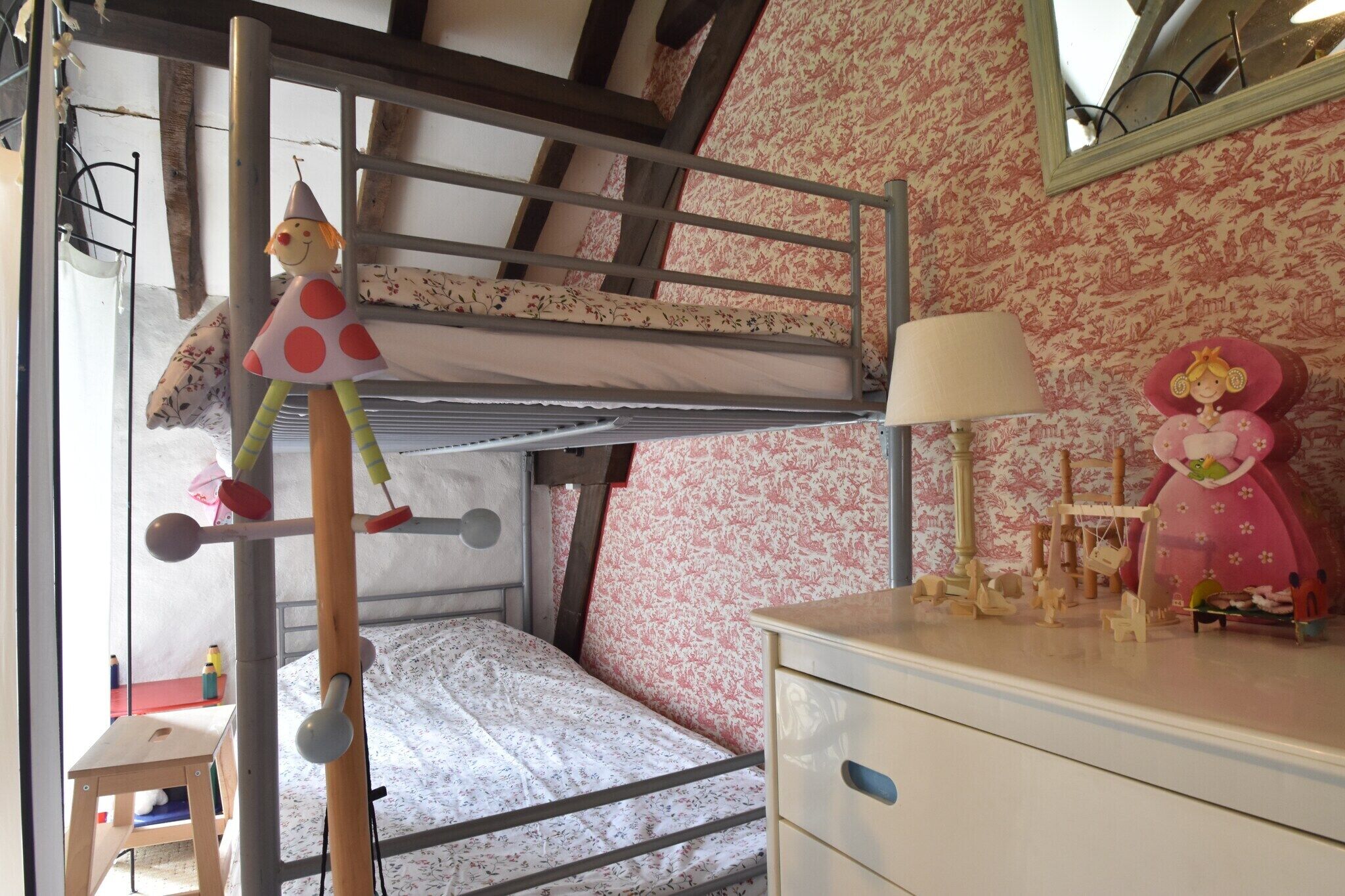 Un lit superposé avec une échelle, une petite table avec une lampe et une commode avec un miroir.