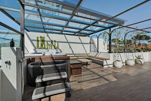 A rooftop terrace with a glass enclosure, outdoor seating, and potted plants.