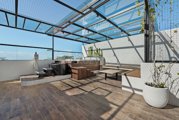 Una terraza moderna en la azotea con techo de vidrio, piso de madera y mobiliario exterior.